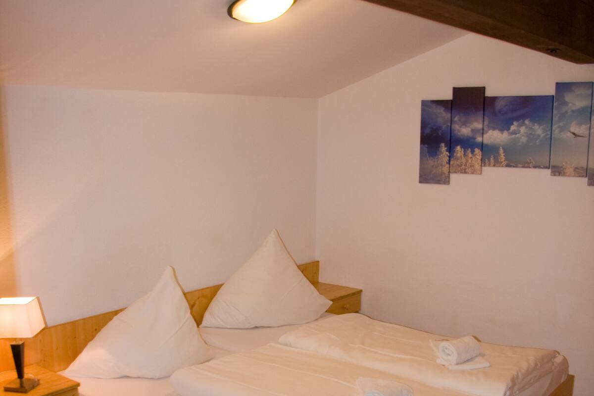 Un lit en bois avec du linge de lit blanc et des oreillers, une table de chevet avec une lampe et un luminaire au plafond.