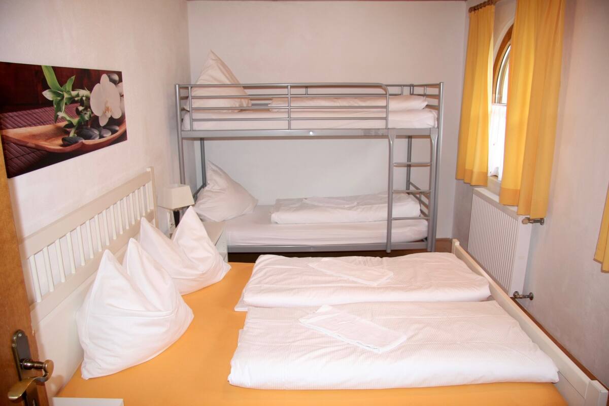 Une chambre avec un lit superposé, une couette blanche, des oreillers et un tableau encadré au mur.