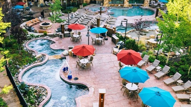Un resort con una amplia piscina exterior, varias zonas de descanso con sombrillas y un jacuzzi.