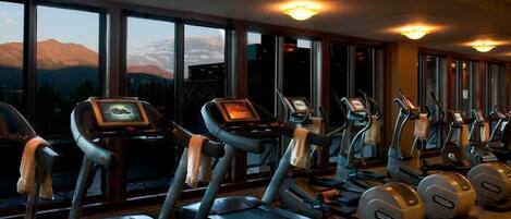A gym with treadmills and ellipticals, large windows with a mountain view, and ceiling lights.