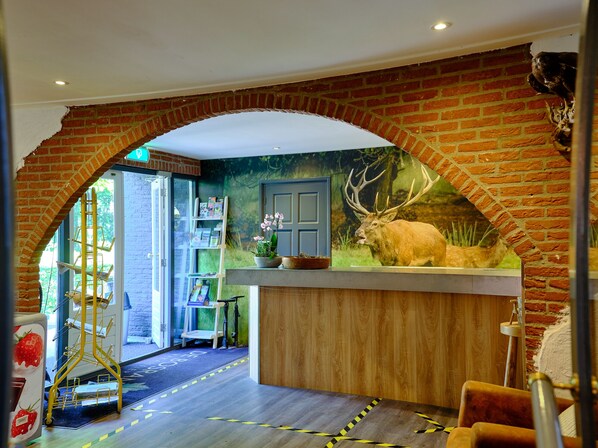 A reception area with a brick archway, a deer mural, a wooden reception desk, and a bookshelf with magazines. - Vakantiepark De Bosrand (Vaassen)