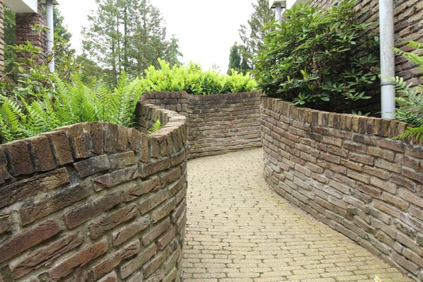 Un étroit sentier pavé de briques, bordé d’un côté par un mur de briques et de l’autre par un mur de briques recouvert de verdure.
