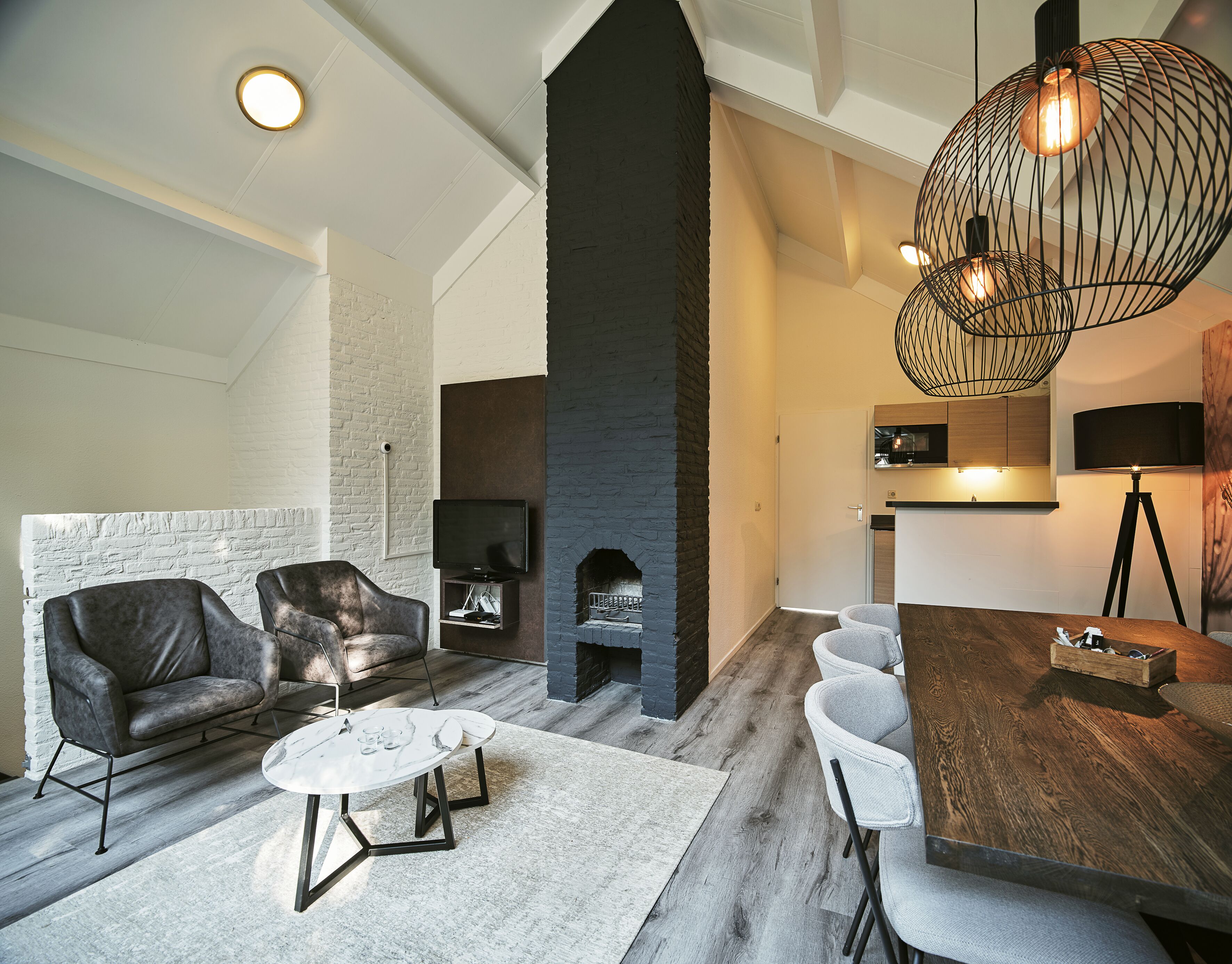 Een moderne woonkamer met een open haard, leren banken, een salontafel, en een eethoek met een houten tafel en stoelen.
