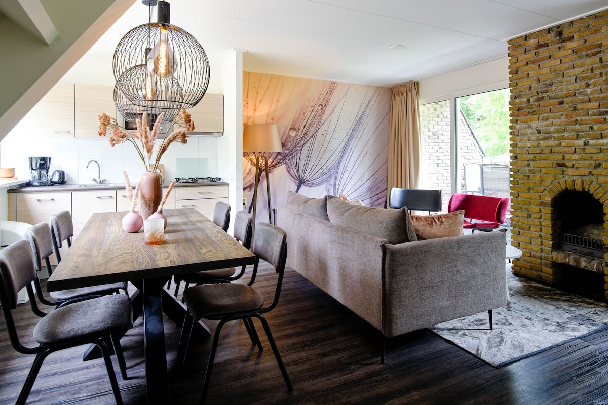 A modern living room with a wooden dining table, grey sofa, and a brick fireplace.