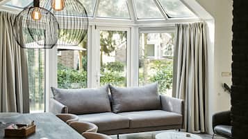 Een moderne woonkamer met een grijze bank, een ronde salontafel en een eettafel met stoelen.