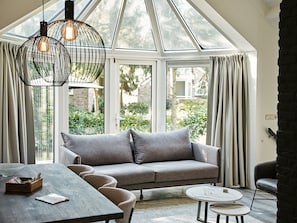Een moderne woonkamer met een grijze bank, een ronde salontafel en een eettafel met stoelen.