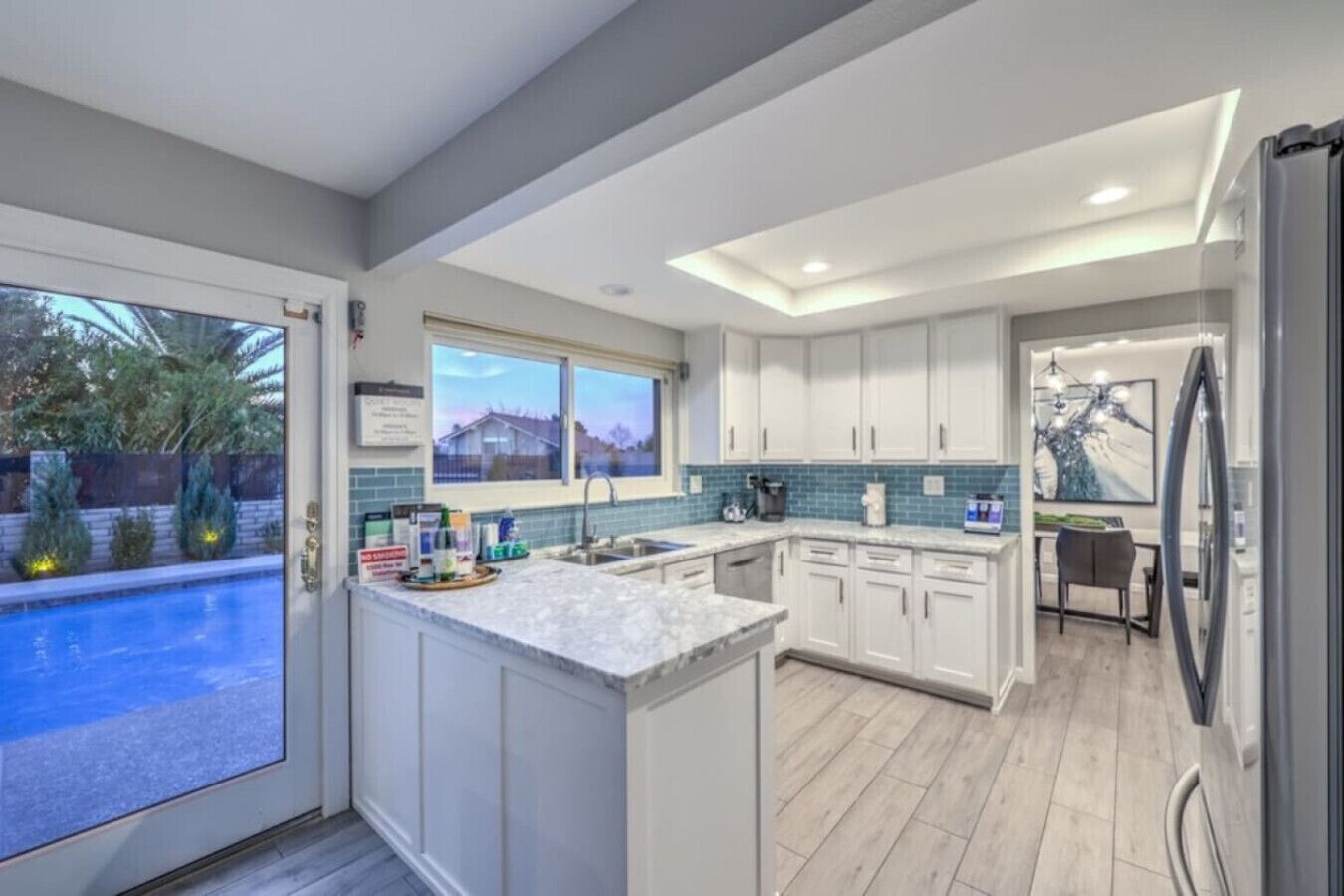 Una cocina moderna con armarios blancos, encimera de mármol y vistas a una piscina.