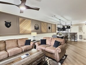 En rummelig stue med et beige sofasæt, et træsofabord og et spiseområde med et køkken i baggrunden.