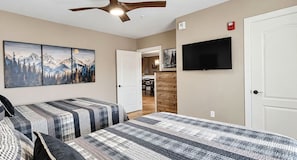 A bedroom with two beds, a ceiling fan, a TV, and a door leading to a bathroom. - Downtown Gatlinburg Luxury Penthouse, Mountain Views & 2 Balconies (Gatlinburg)