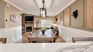 A spacious dining area with a long wooden table, a fireplace, and a stone accent wall.
