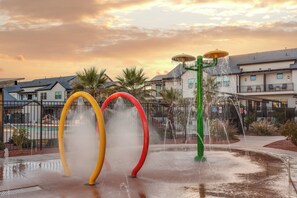 A water play area with colorful water jets, surrounded by residential buildings and palm trees.