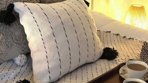 En pænt redt seng med et stribet tæppe, to puder og et bakke med croissanter og kaffekopper.