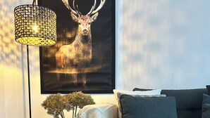 En hyggelig stue med en mørk sofa, et billede af et rådyr i ramme, en gulvlampe og pynteting på et sofabord.