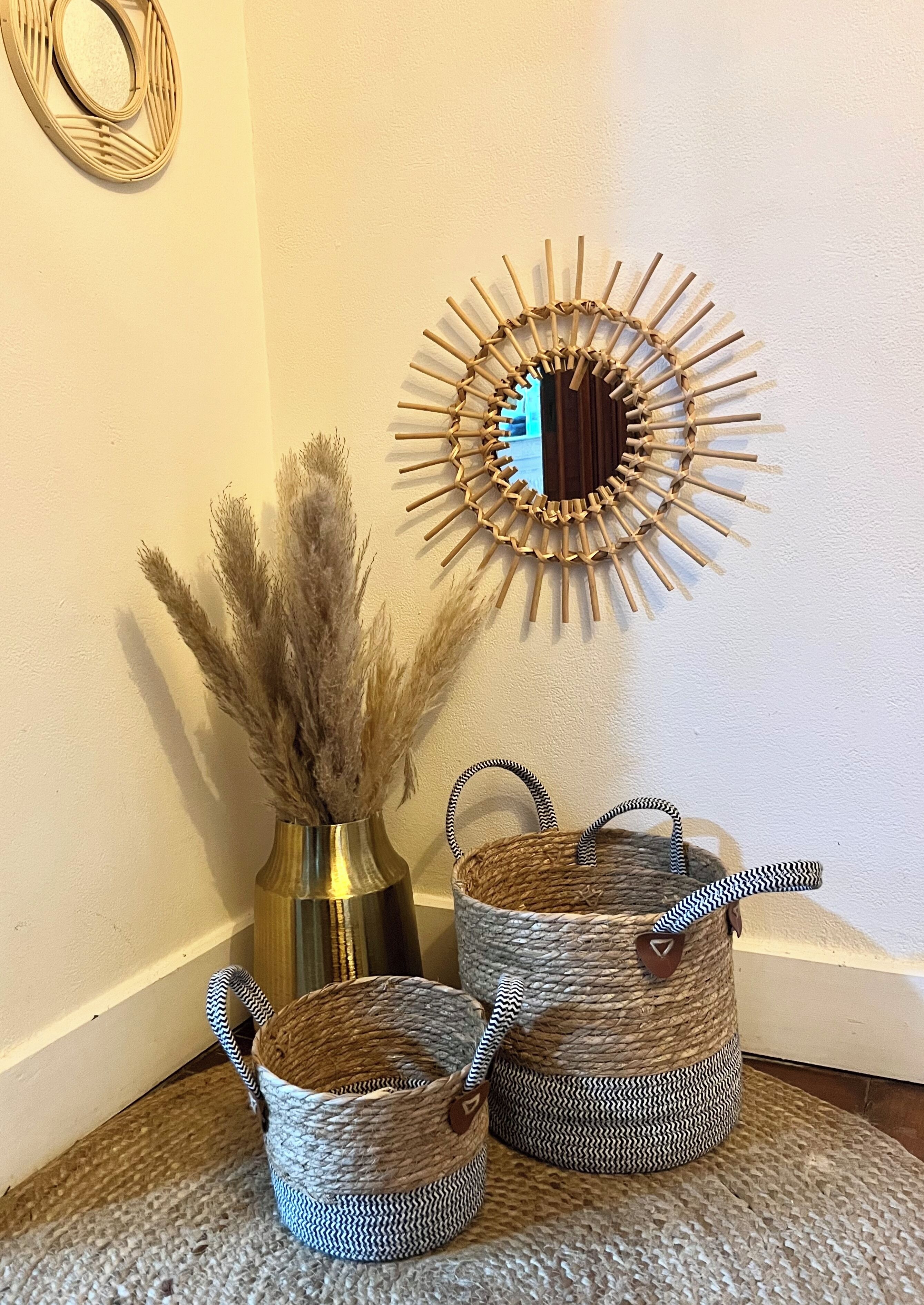 Eine Ecke mit einem gewebten Korb, einer Metallvase mit Pampasgras und einem spiegelnden Wandbild.