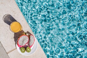 A poolside view with a plate of dragon fruit and kiwi slices, and a glass of orange juice.