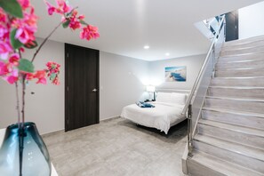 A hotel room with a bed, a nightstand, a lamp, a painting, and a staircase.