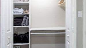 Een inloopkast met witte deuren, planken voor opgevouwen kleding en een kledingroede.