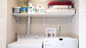 Een praktische wasruimte met een voorlader wasmachine en droger, een plank met schoonmaakmiddelen en een klein wit kastje.