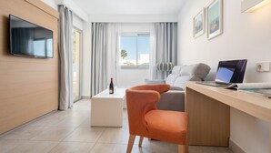 Quarto de hotel moderno com televisão de tela plana, escrivaninha com laptop, sofá confortável e vista para o exterior.