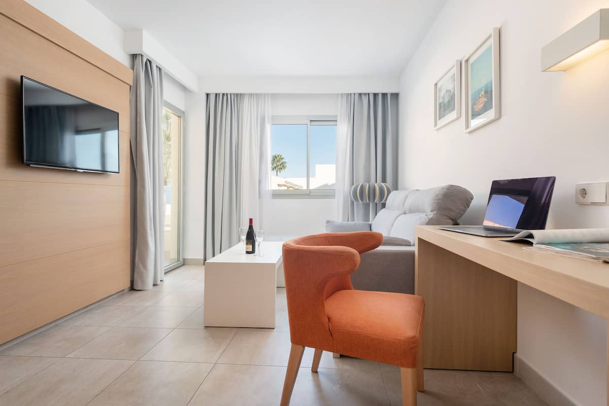 Une chambre d’hôtel moderne dotée d’une télévision à écran plat, d’un bureau avec un ordinateur portable, d’un canapé confortable et offrant une vue sur l’extérieur.