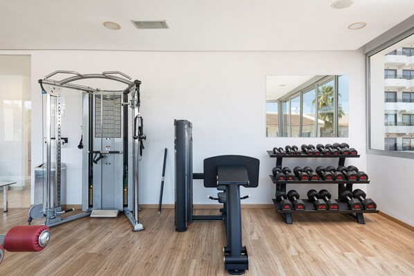 Un gimnasio con diversos equipos, incluyendo una máquina de poleas, una estructura para sentadillas y un banco de pesas.