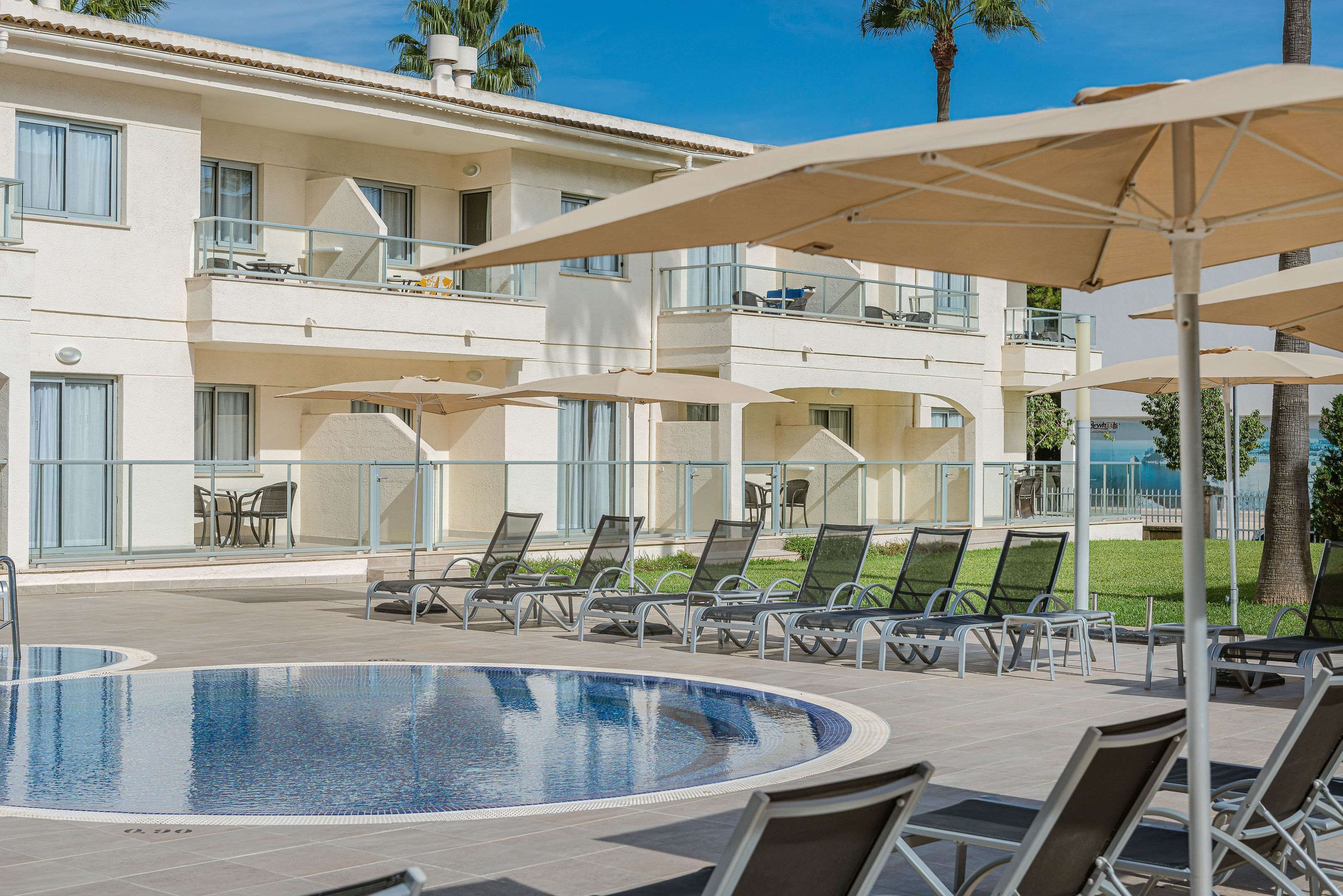 A hotel with a pool area, sun loungers, and umbrellas.