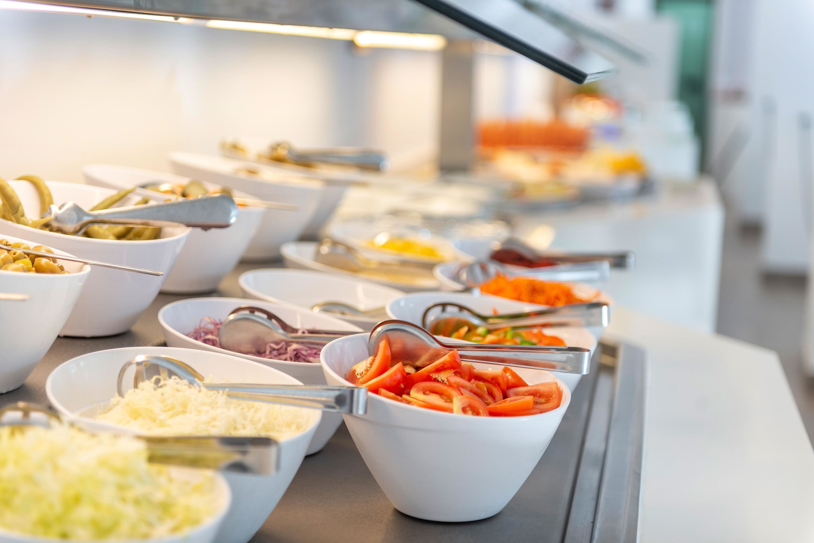 Buffet com diversos alimentos em recipientes, incluindo tomates fatiados e queijo ralado.