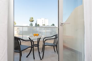 Un balcon avec une table et deux chaises, donnant sur un paysage urbain avec des palmiers et des immeubles.