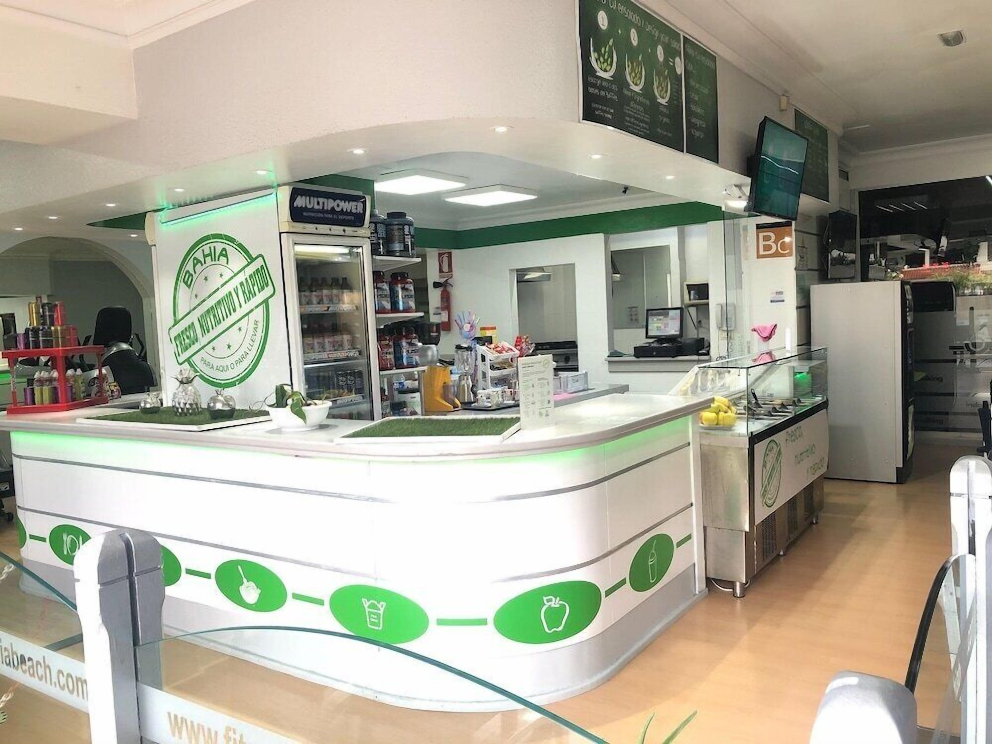 Un stand de restauration aux couleurs verte et blanche, équipé d’un réfrigérateur, d’étagères remplies de produits et d’un comptoir où est affiché le menu.