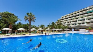 Una piscina amb dues persones nedant, envoltada de palmeres i gandules.