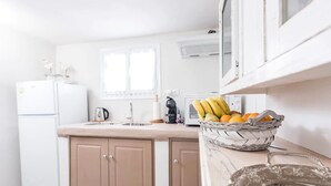 A kitchen with white cabinets, a refrigerator, a microwave, and a fruit basket on the counter.