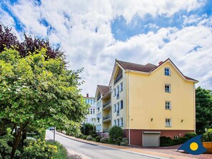 Un immeuble résidentiel à plusieurs étages, doté d’une façade jaune, de nombreux balcons et d’un toit recouvert de tuiles rouges.