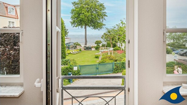 A view from a balcony with a large tree, a lawn, and a body of water in the background.