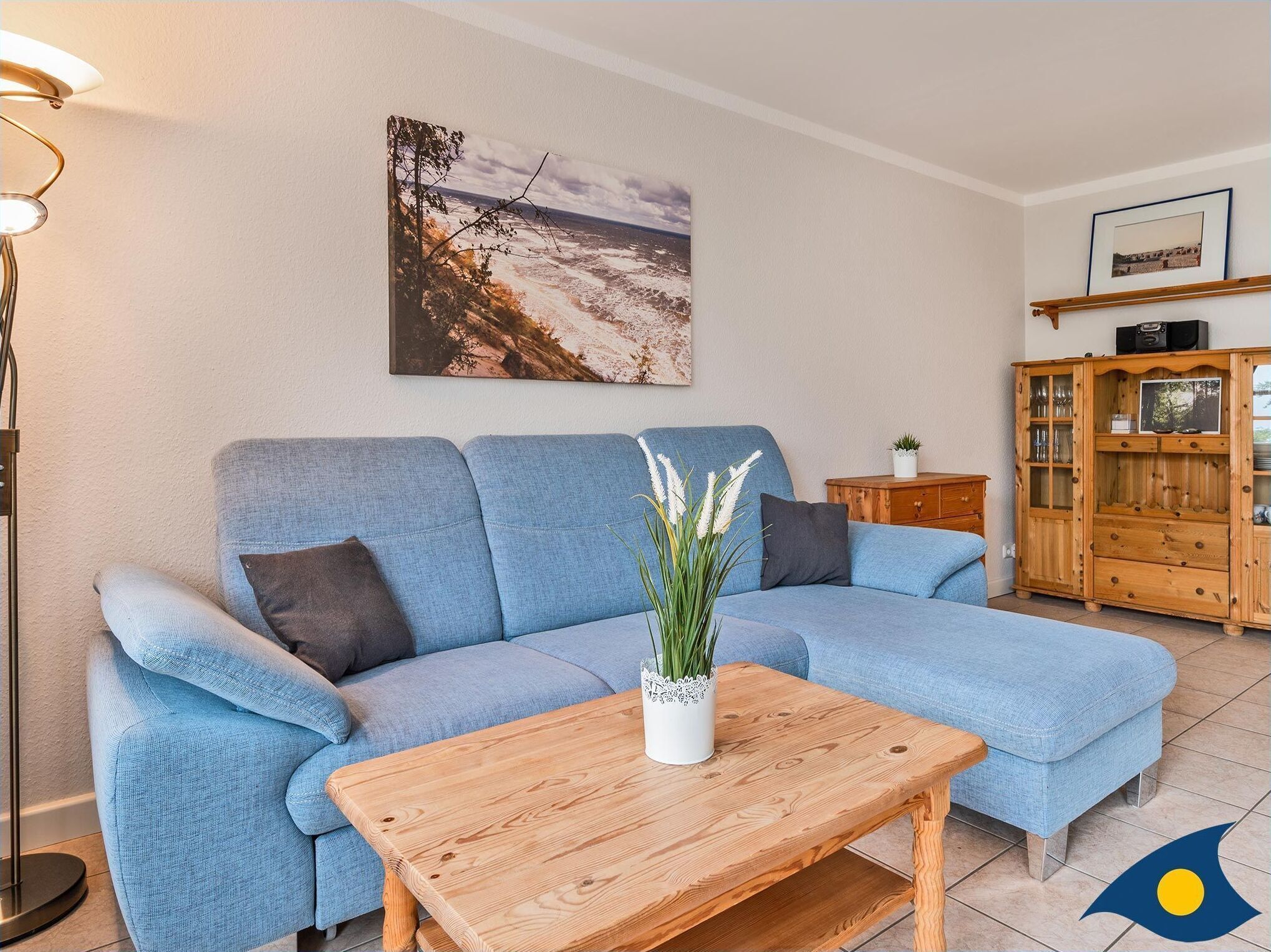 A living room with a blue sofa, a wooden coffee table, a floor lamp, a painting, and a wooden cabinet.