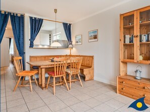 A dining area with a wooden table and chairs, a hanging lamp, and a wooden cabinet with books. - Rolandseck II, Whg. 07 - RO II 07 (Heringsdorf)