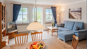 A cozy living room with a wooden dining table, a blue sofa, and a television on a wooden stand.