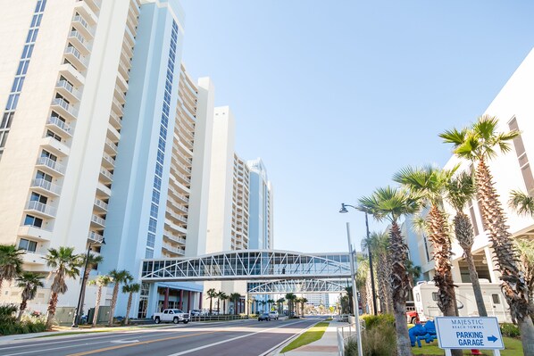 A modern hotel with a prominent glass bridge structure, high-rise buildings, and a parking garage sign.