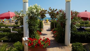 Un sendero que lleva a una zona de playa con sombrillas y sillas, rodeado de follaje y flores.