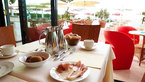 Una mesa lista para el desayuno, con un tazón de fresas, un plato de jamón, una cafetera y una taza de café.