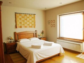 Een slaapkamer met een houten bed, een nachtkastje, een raam met zonwering en een radiator.