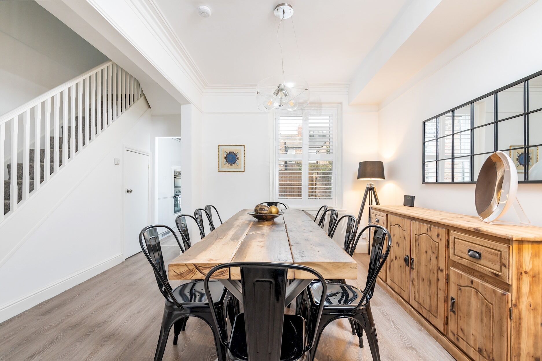 Un espace repas comprenant une longue table en bois, des chaises en métal noir et un buffet en bois doté de tiroirs.