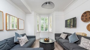 Ein modernes Wohnzimmer mit zwei grauen Sofas, einem runden Couchtisch und einem großen Fenster mit Jalousien.