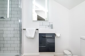 Ein modernes Badezimmer mit Duschabtrennung aus Glas, einem weißen Waschbecken mit schwarzem Unterschrank und einer weißen Toilette.