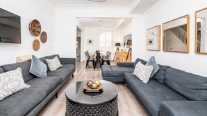 Ein modernes Wohnzimmer mit zwei grauen Sofas, einem runden Couchtisch und einem Essbereich mit Holztisch und Stühlen.