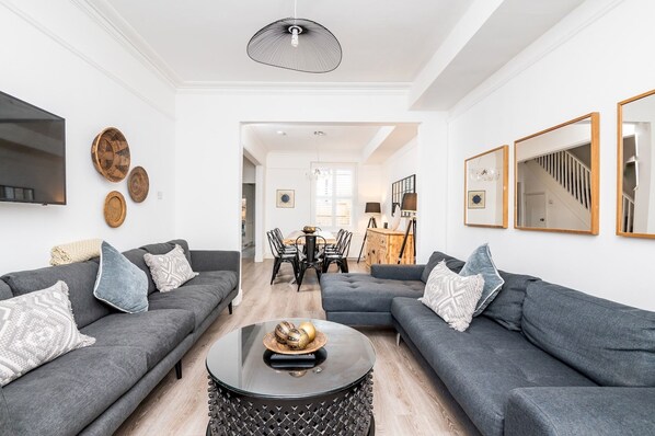 A modern living room with two grey sofas, a round coffee table, and a dining area with a wooden table and chairs. - 6 Longfield Terrace · Elegant, Modern 5 Bed House with Free Parking - Pass The Keys (York)