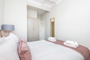 A bedroom with a bed, a wardrobe, a mirror, and a lamp. - 6 Longfield Terrace · Elegant, Modern 5 Bed House with Free Parking - Pass The Keys (York)
