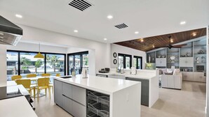 A modern kitchen with a central island, yellow chairs, and a dining area with a view. - Villa by the Sea🌴  🌊  Luxury Coastal Retreat - 5 Minute walk to beach (Lauderdale by the Sea)