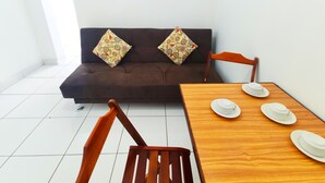 A room with a dark brown sofa, two patterned cushions, a wooden dining table with white plates and cups, and wooden chairs. - TC202 Paraíso na Praia (Rio de Janeiro)