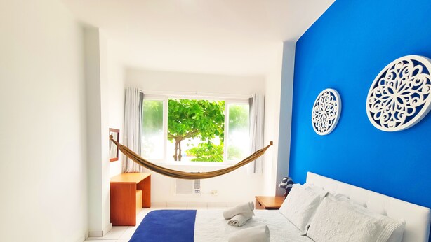 A bedroom with a bed, a hammock, a view of greenery outside, and decorative wall art. - TC202 Paraíso na Praia (Rio de Janeiro)