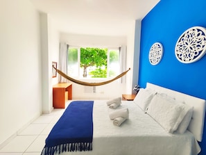Ein Schlafzimmer mit Bett, einer Hängematte, Blick auf Grünflächen und dekorativen Wandbildern.